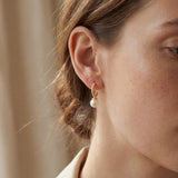Model wearing a small gold half hoop earring with a white freshwater pearl drop