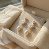 Pair of white camellia pearl earrings presented inside a cream jewelry box