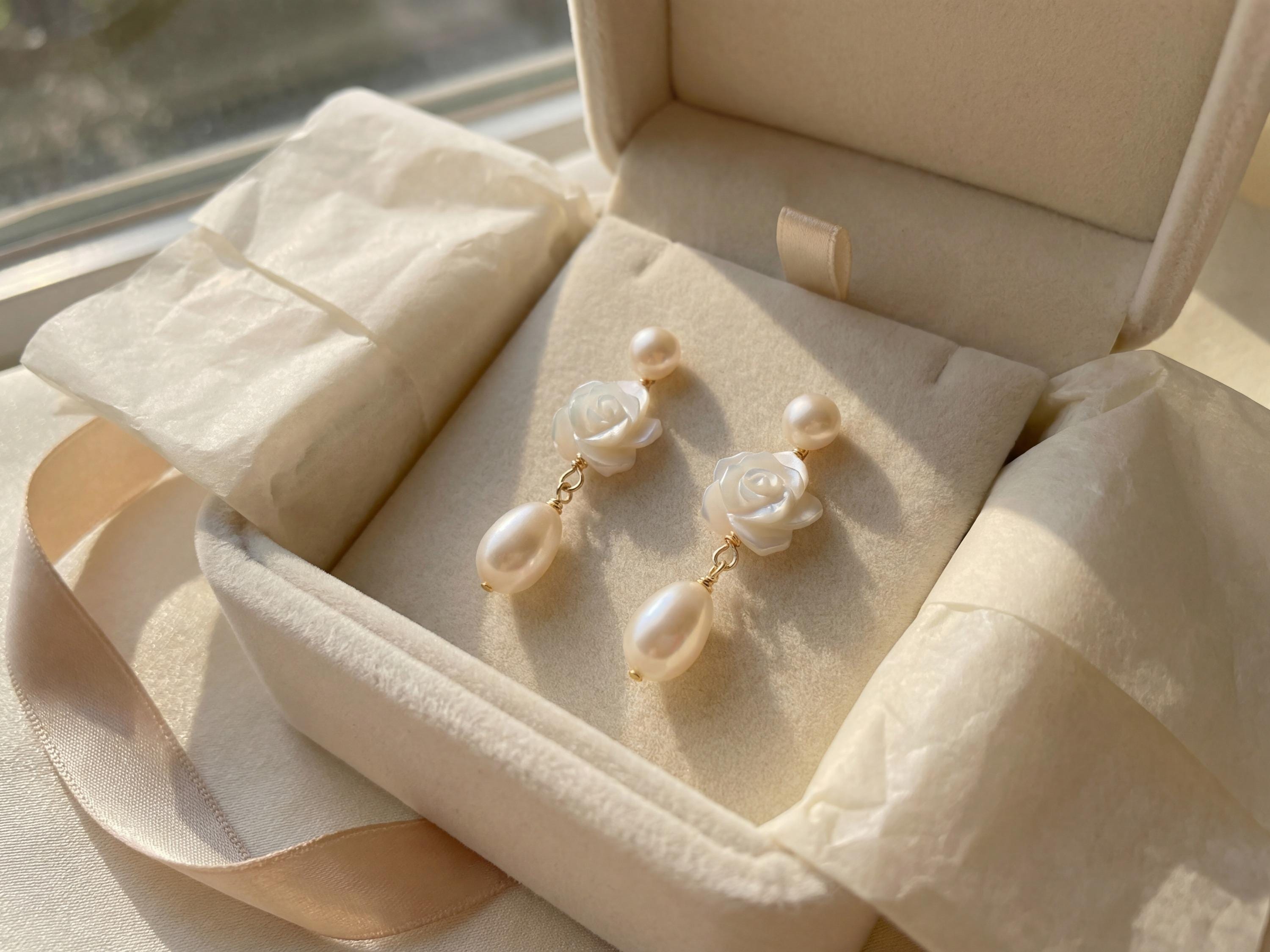 Pair of white camellia pearl earrings presented inside a cream jewelry box