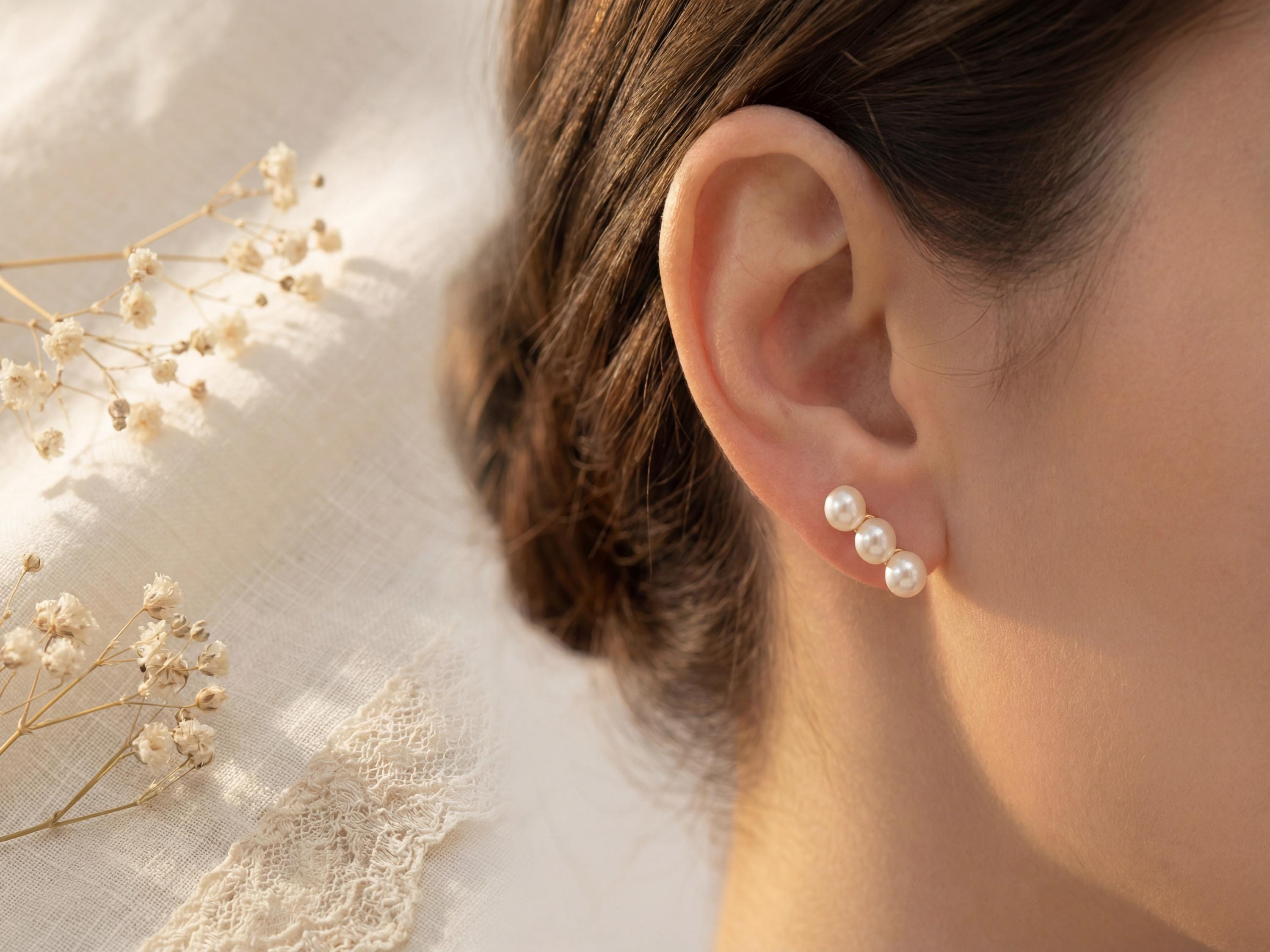 Triple pearl gold leverback earring worn beside dried white flowers