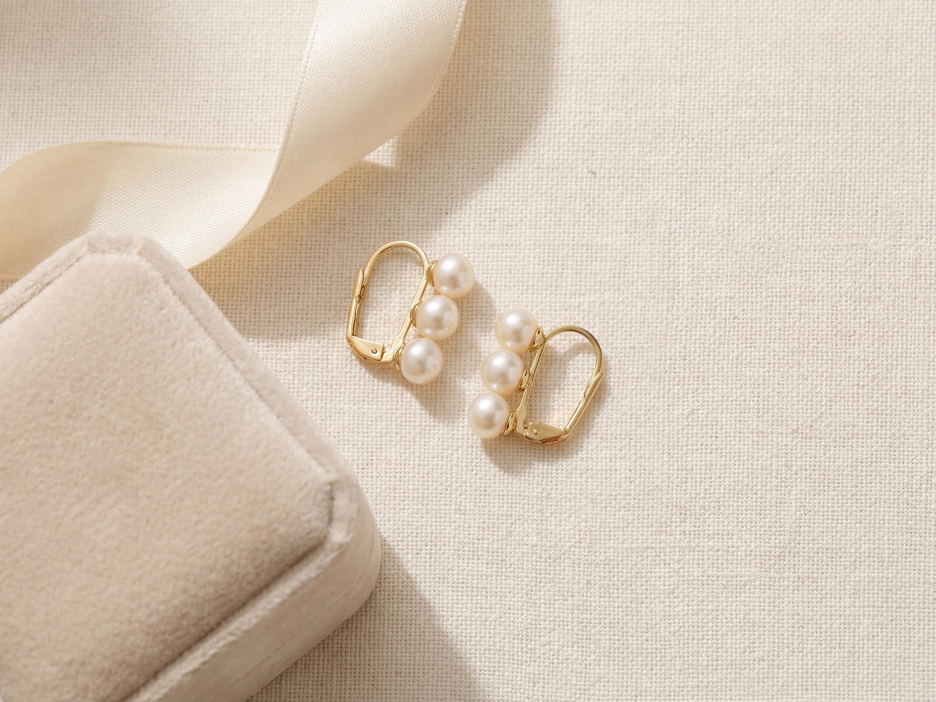 Gold triple pearl earrings arranged beside a cream jewelry gift box