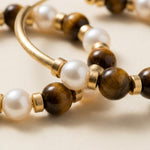 Close up of tiger eye gemstone beads, freshwater pearls, and warm gold tone spacers