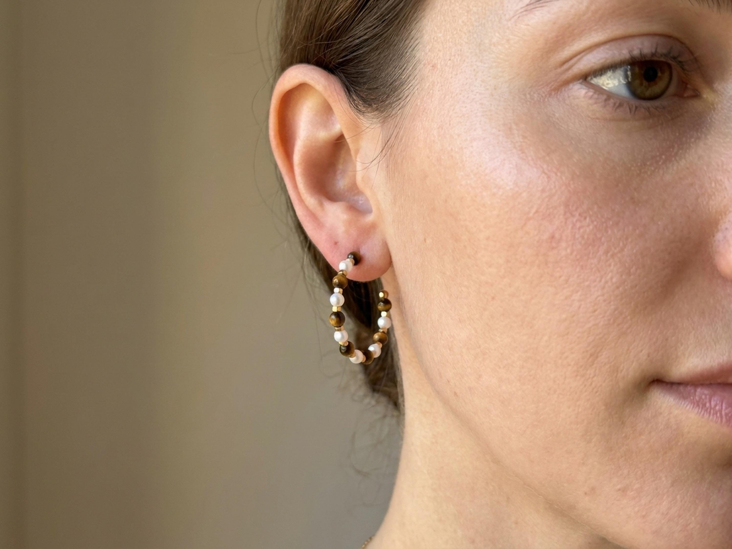 Tiger eye pearl hoop earrings worn on ear with brown gemstone beads, white pearls, and gold tone accents