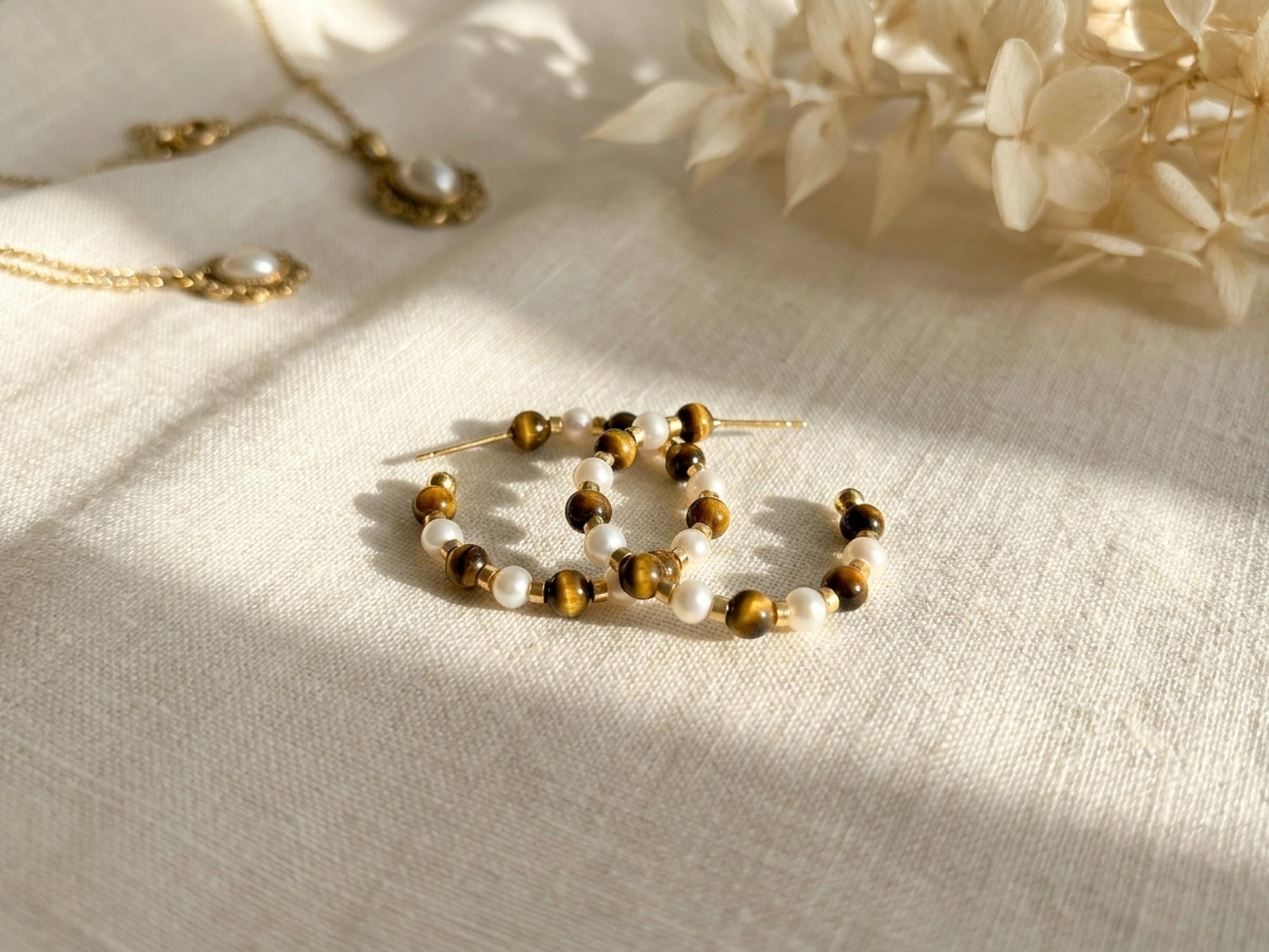 Tiger eye and freshwater pearl hoop earrings styled on cream fabric in warm natural light