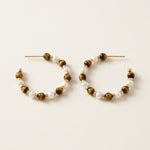 Pair of tiger eye and white pearl beaded hoop earrings on a neutral cream background