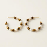 Pair of tiger eye and white pearl beaded hoop earrings on a neutral cream background