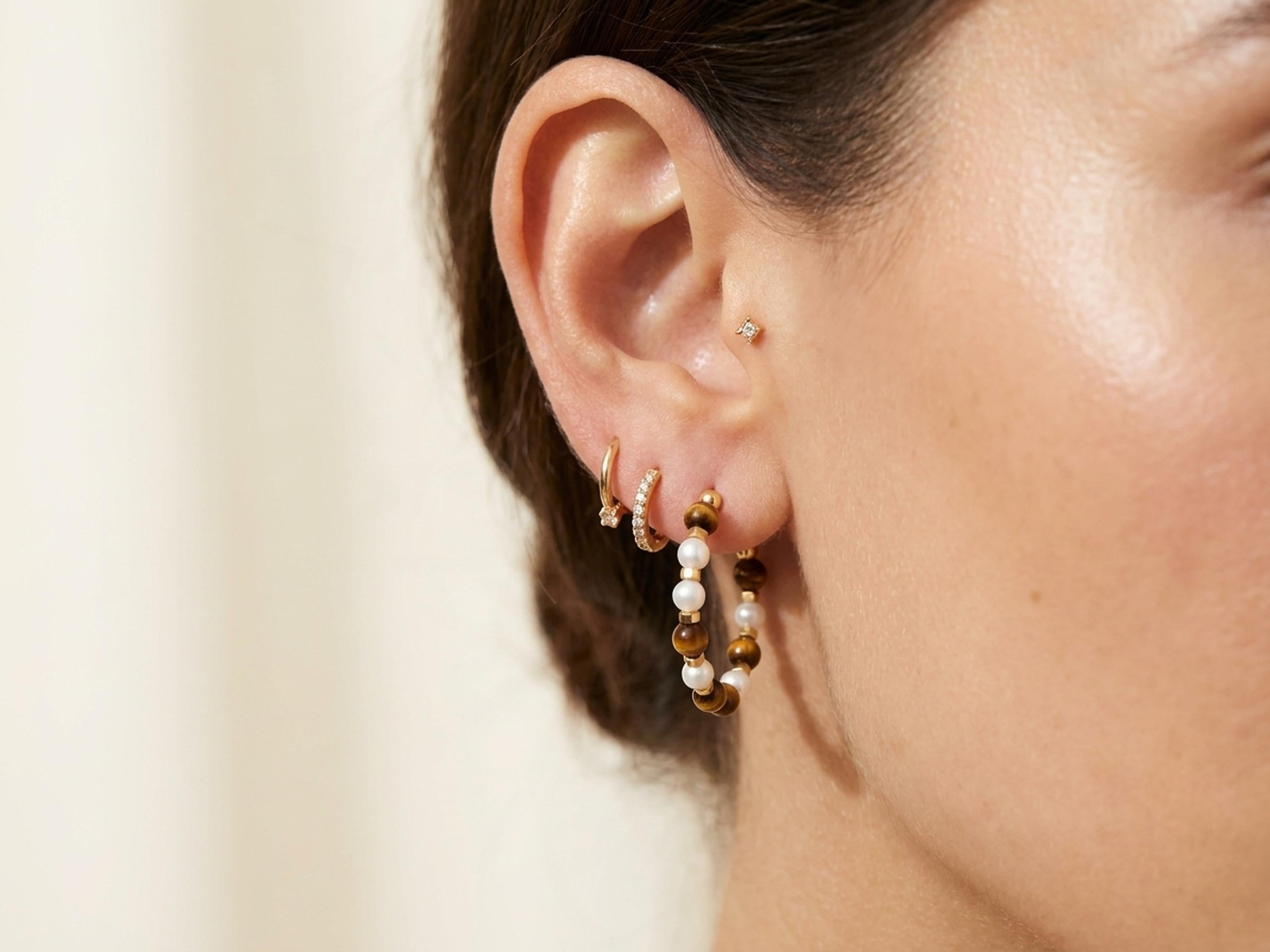 Tiger eye pearl hoop earrings styled with warm gold jewelry for a layered look