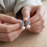 Hands holding matching blue oval cubic zirconia and white pearl drop earrings