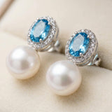 Close-up of oval blue cubic zirconia halo stud earrings with white pearl drops