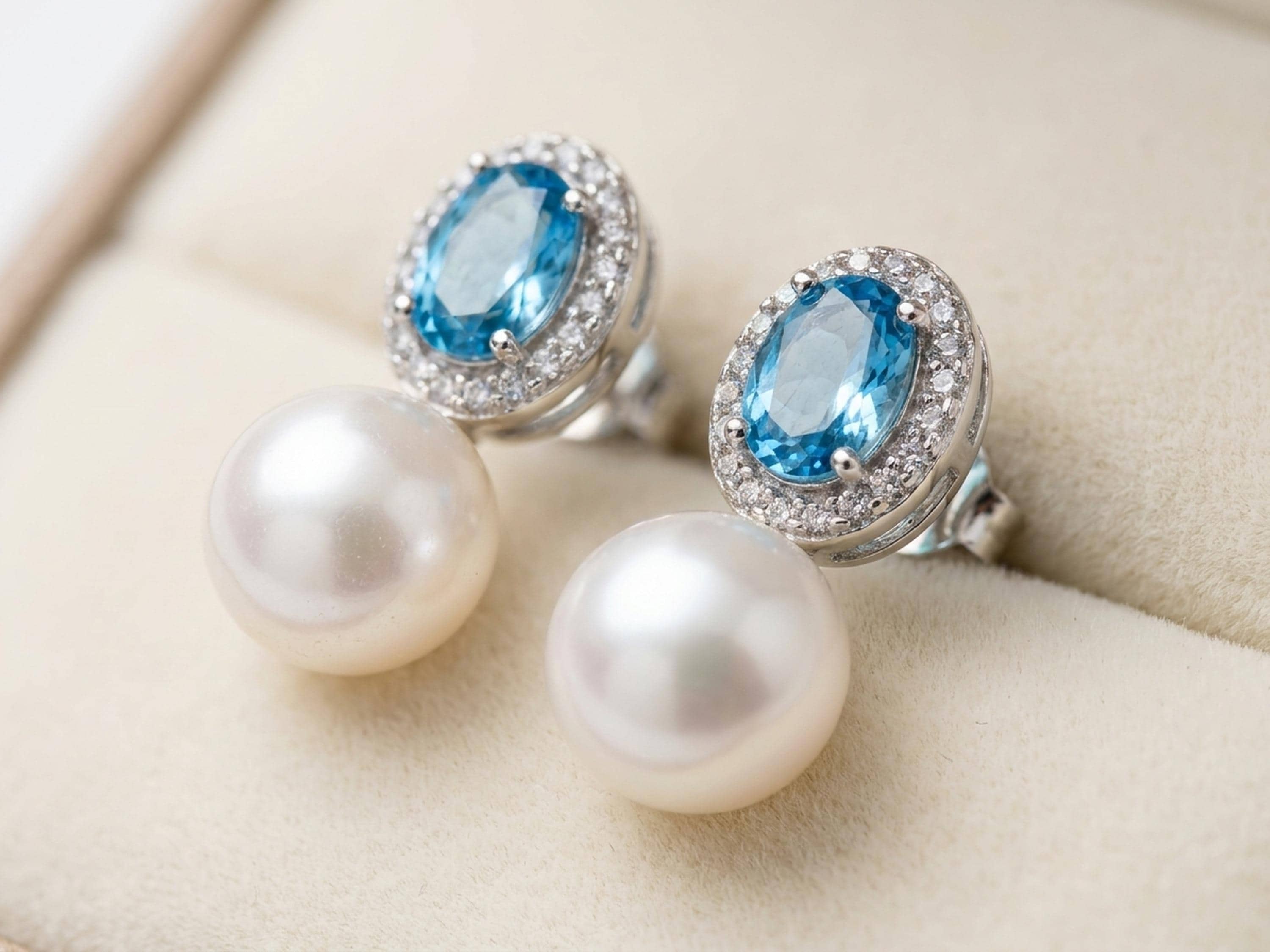 Close-up of oval blue cubic zirconia halo stud earrings with white pearl drops