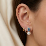 Side view of blue cubic zirconia and pearl drop earrings worn with small gold hoops