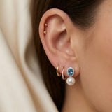 Side view of blue cubic zirconia and pearl drop earrings worn with small gold hoops