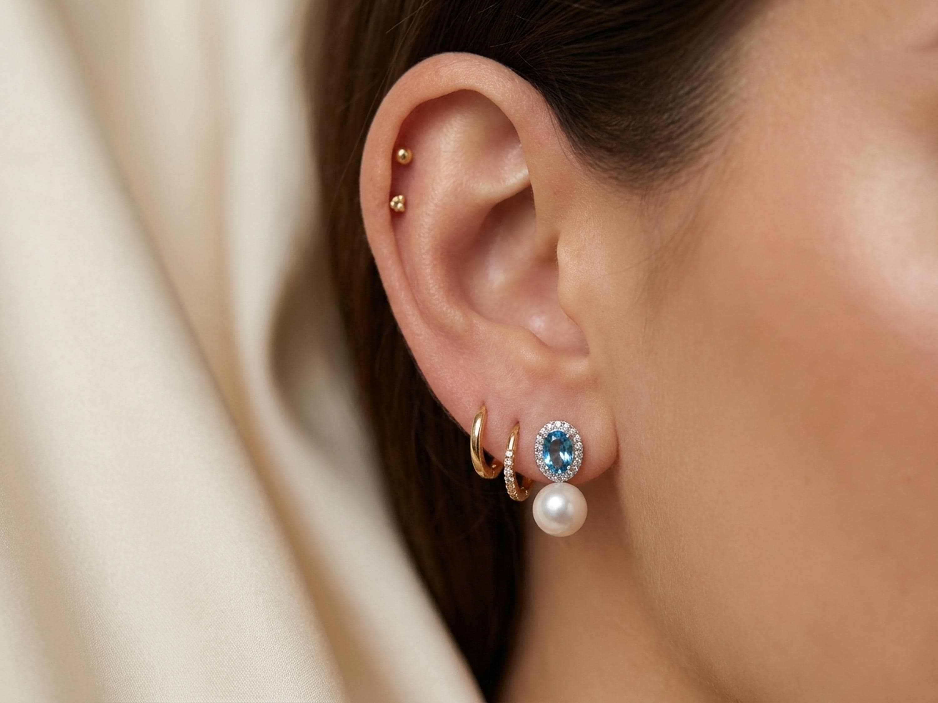 Side view of blue cubic zirconia and pearl drop earrings worn with small gold hoops