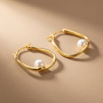 Close-up of sculptural 14K gold plated silver hoop earrings with round freshwater pearl accents and hinged closures