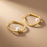 Close-up of sculptural 14K gold plated silver hoop earrings with round freshwater pearl accents and hinged closures