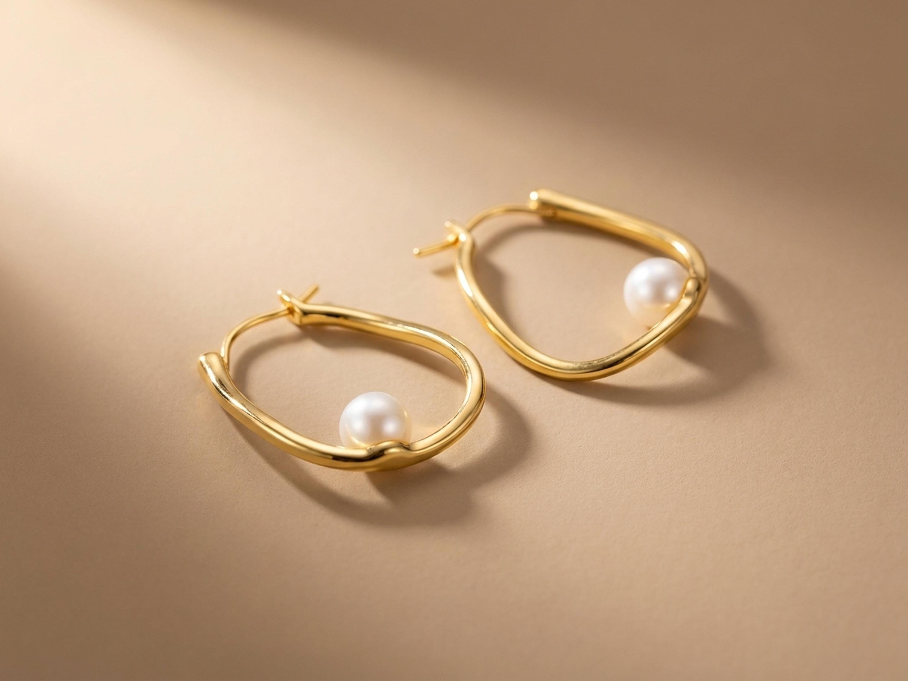 Close-up of sculptural 14K gold plated silver hoop earrings with round freshwater pearl accents and hinged closures