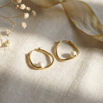 Side profile of a model wearing sculptural 14K gold plated oval hoop earrings with white freshwater pearls