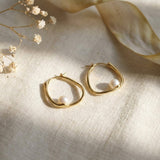 Side profile of a model wearing sculptural 14K gold plated oval hoop earrings with white freshwater pearls