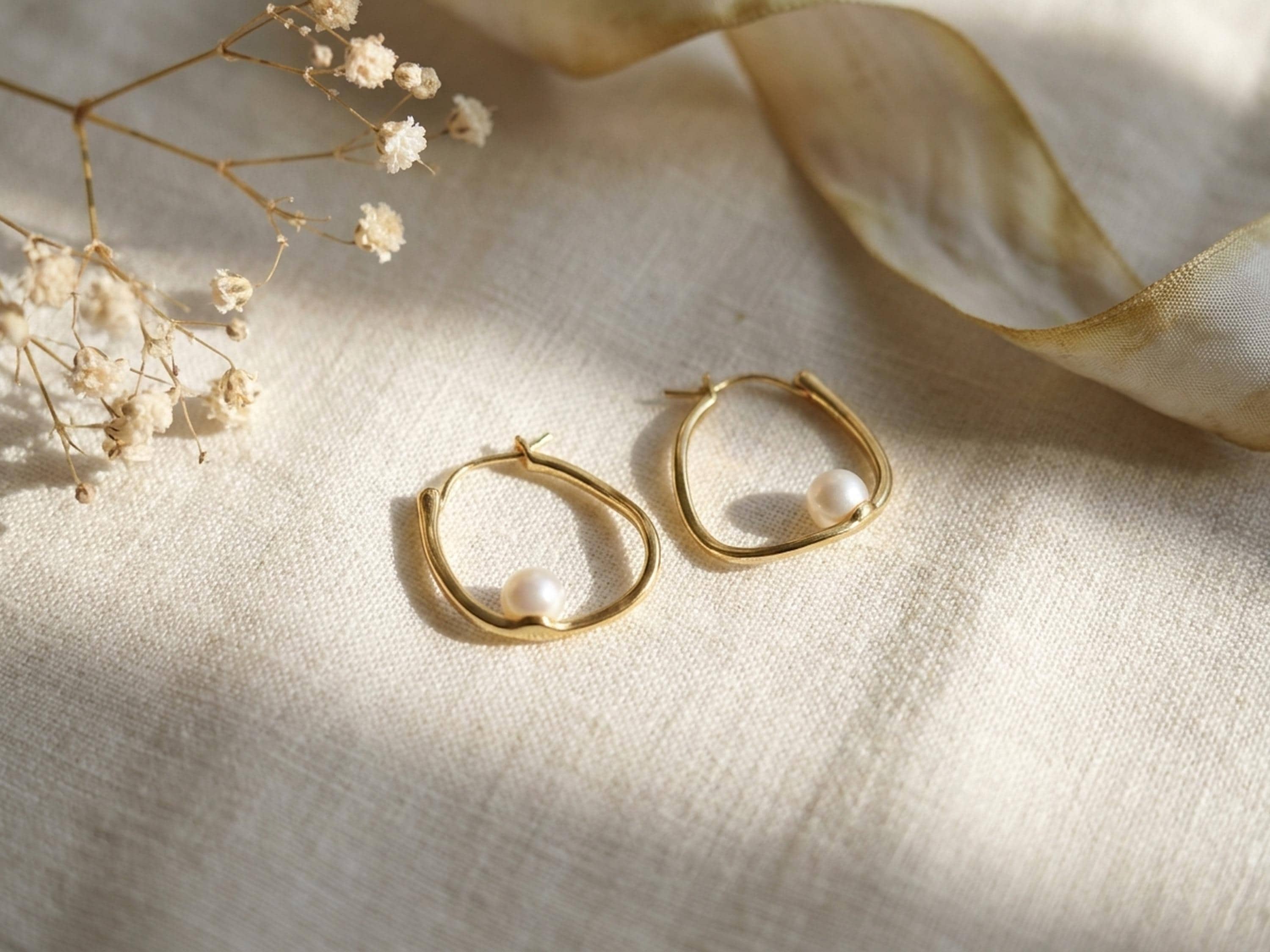 Side profile of a model wearing sculptural 14K gold plated oval hoop earrings with white freshwater pearls