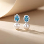 Blue cubic zirconia and white pearl drop earrings standing on a neutral beige background