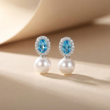Blue cubic zirconia and white pearl drop earrings standing on a neutral beige background