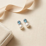 Blue cubic zirconia pearl drop earrings styled beside ribbon and a jewelry box