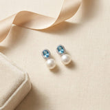 Blue cubic zirconia pearl drop earrings styled beside ribbon and a jewelry box
