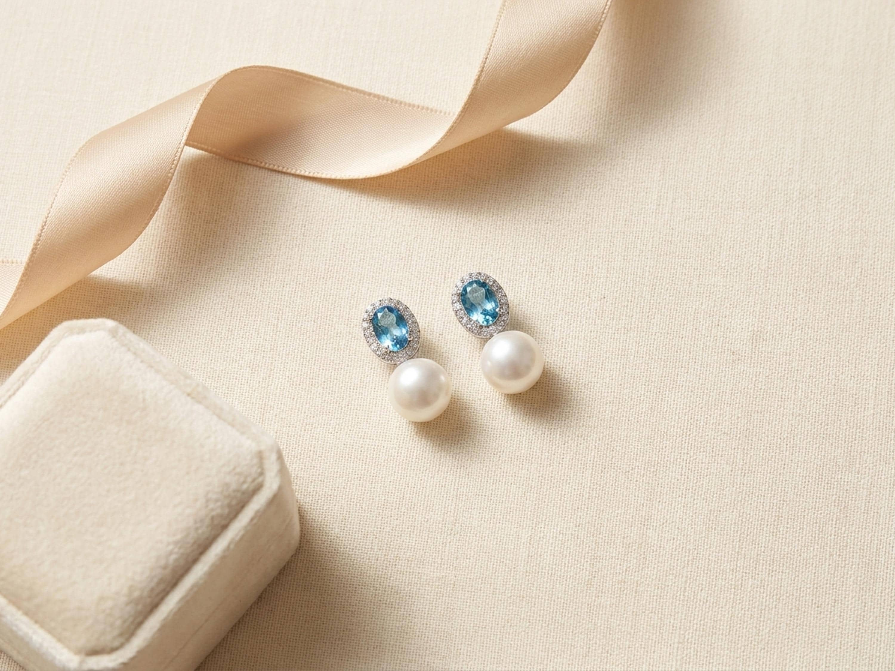 Blue cubic zirconia pearl drop earrings styled beside ribbon and a jewelry box