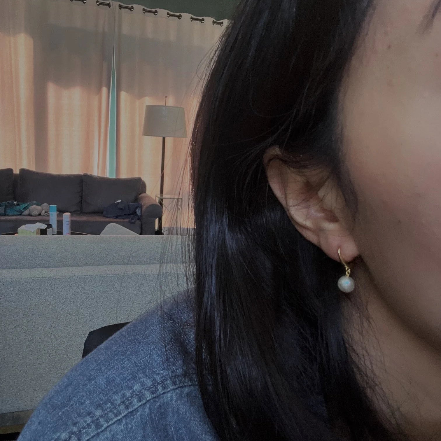 Gold-plated hoop earring with a dangling white freshwater pearl on a person's ear.