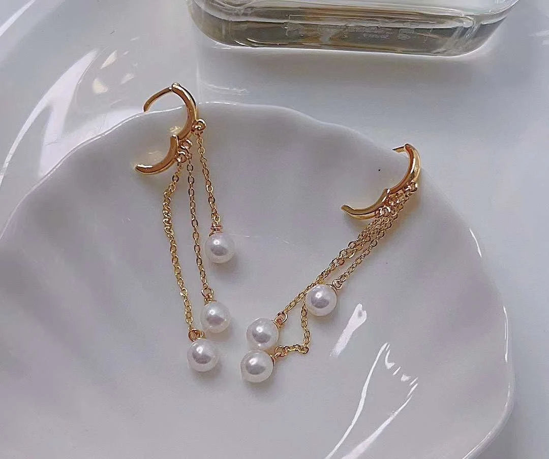 Three pearls tear drop earrings with gold-plated chains on a white surface.