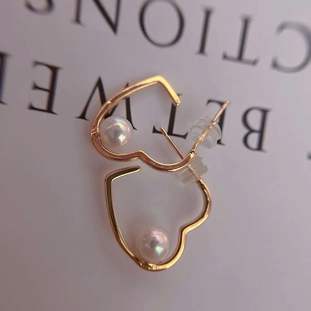 Gold heart-shaped earrings with freshwater pearls, one with a clear silicone backing.