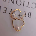 Gold heart-shaped earrings with freshwater pearls, one with a clear silicone backing.
