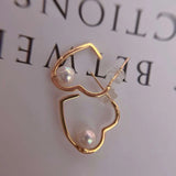 Gold heart-shaped earrings with freshwater pearls, one with a clear silicone backing.