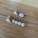Mismatched gold-plated earrings with one large pearl and four smaller pearls on a wooden surface.