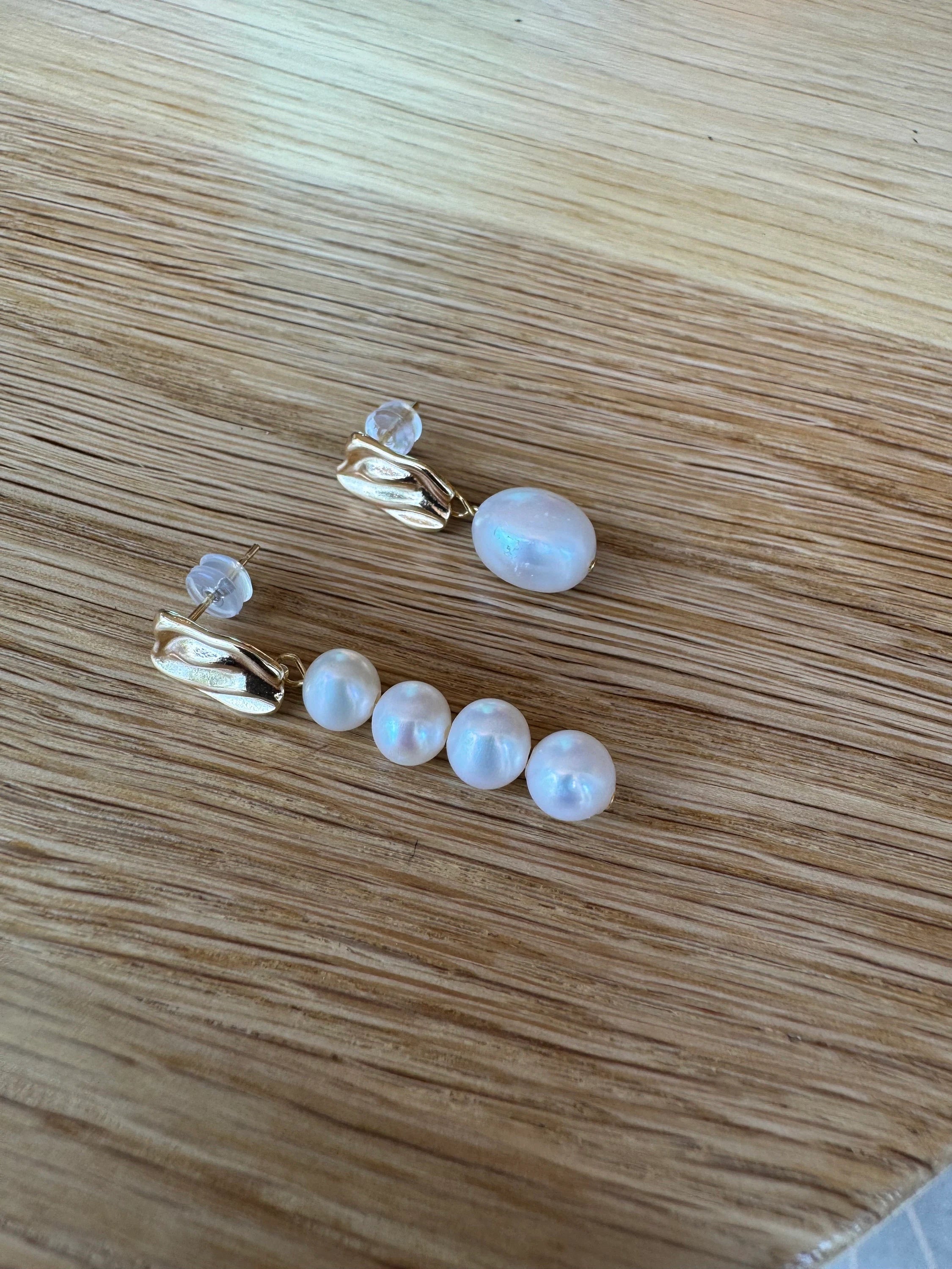 Mismatched gold-plated earrings with one large pearl and four smaller pearls on a wooden surface.