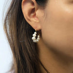A woman wears a gold hoop earring with freshwater pearls on her right ear.