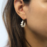 A woman wears a gold hoop earring with freshwater pearls on her right ear.