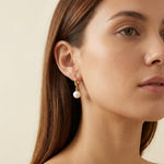 A model wears Caellia 14K gold hoop earrings featuring a dangling freshwater pearl.