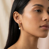 A model wears Caellia silver-plated hoop earrings featuring a dangling freshwater pearl.