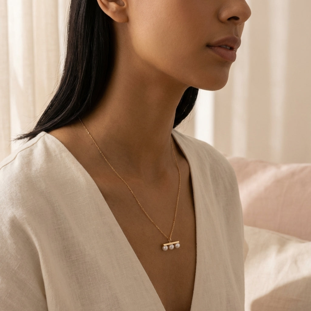 A woman wearing a Caellia 14K gold plated necklace featuring three freshwater pearl pendants.