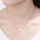 A dainty freshwater pearl pendant necklace with a silver chain on a person's neck.