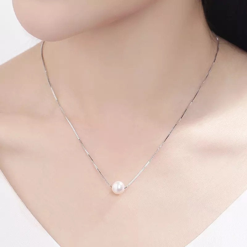A dainty freshwater pearl pendant necklace with a silver chain on a person's neck.