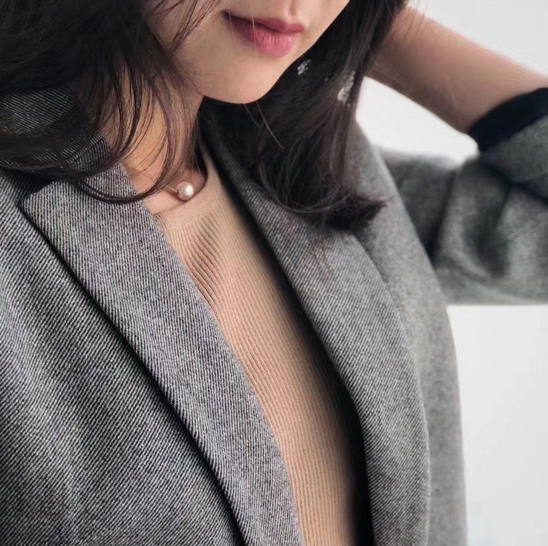 A woman wears a freshwater Edison pearl necklace with a gold chain over a beige top and gray blazer.