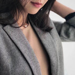 A woman wears a freshwater Edison pearl necklace with a gold chain over a beige top and gray blazer.