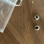 A gold chain necklace with a single freshwater pearl and two silver hoop earrings.