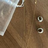 A gold chain necklace with a single freshwater pearl and two silver hoop earrings.