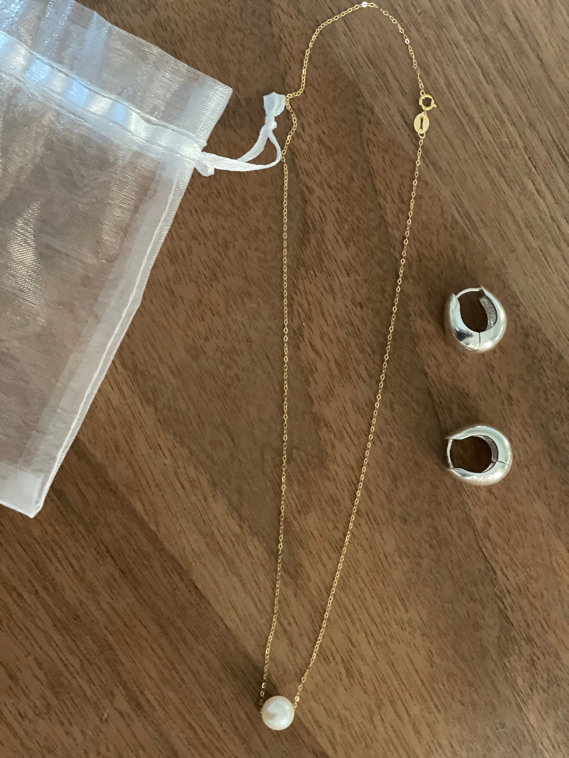 A gold chain necklace with a single freshwater pearl and two silver hoop earrings.