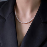 A woman wears a white freshwater pearl necklace with a black blazer.