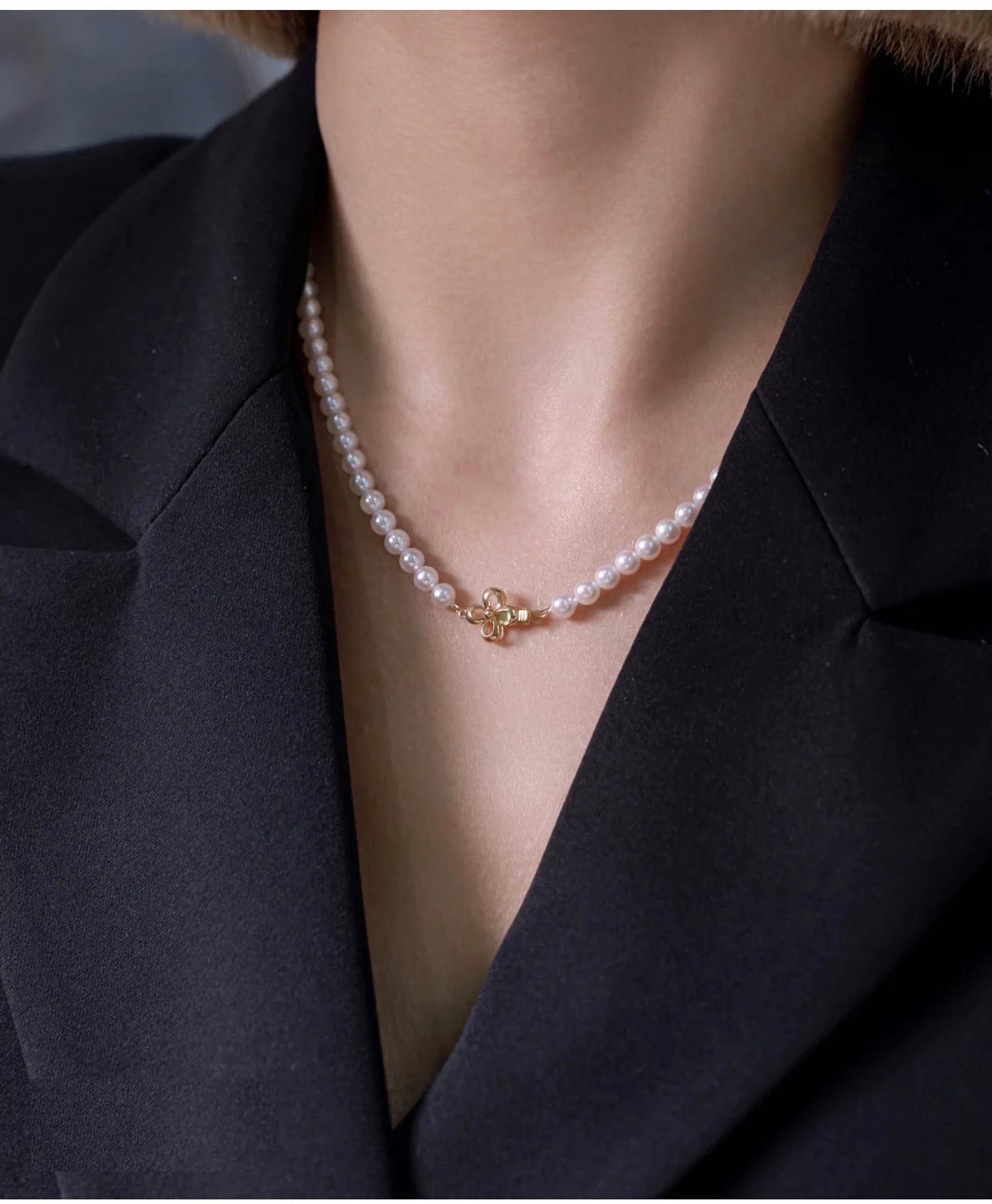 A woman wears a freshwater pearl necklace with an 18K gold clover clasp.