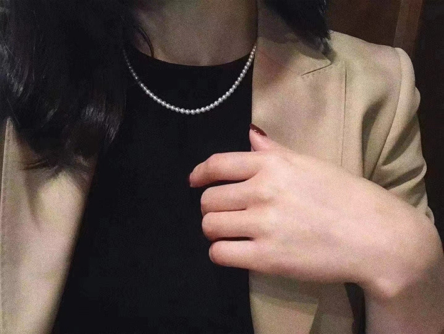 A woman wears a tiny bead pearl necklace over a black top and a beige blazer.